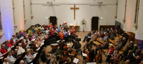 A view of the church from the balcony with singers on the left side, an orchestra in the middle and an audience sitting on the right hand side.